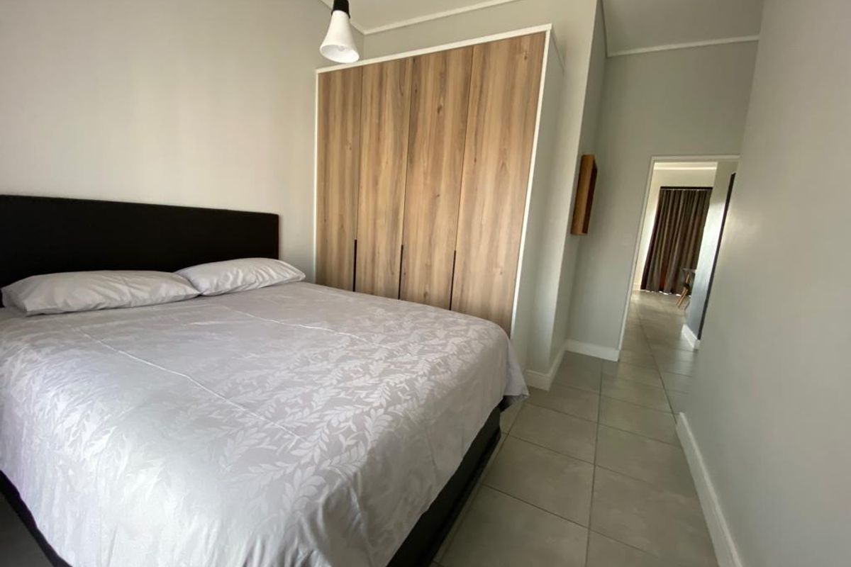 A well-maintained bedroom featuring neutral tiled flooring, a modern built-in wardrobe with wood-grain finish, and a clean, minimalist aesthetic.