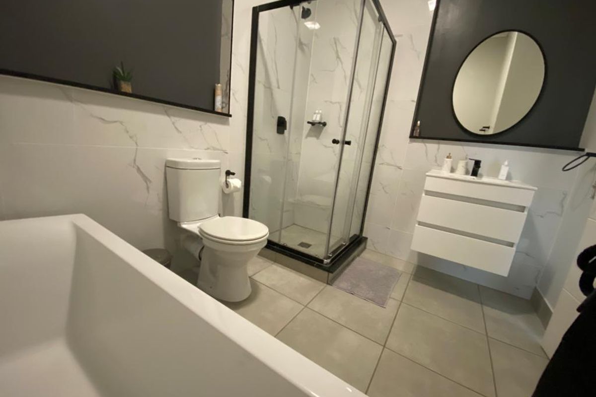 Modern bathroom featuring a walk-in shower with black frame, wall-mounted vanity, and a sleek freestanding bathtub with marble-effect wall tiling.
