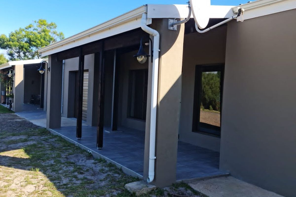 A rear view of the house featuring a covered patio area with tiled flooring, timber support posts, and exterior lighting.