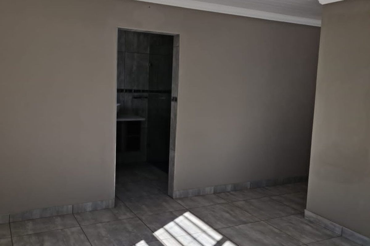 A clean, empty bedroom featuring neutral wall tones, modern tiled flooring, and a tongue and groove ceiling with a central light fixture.
