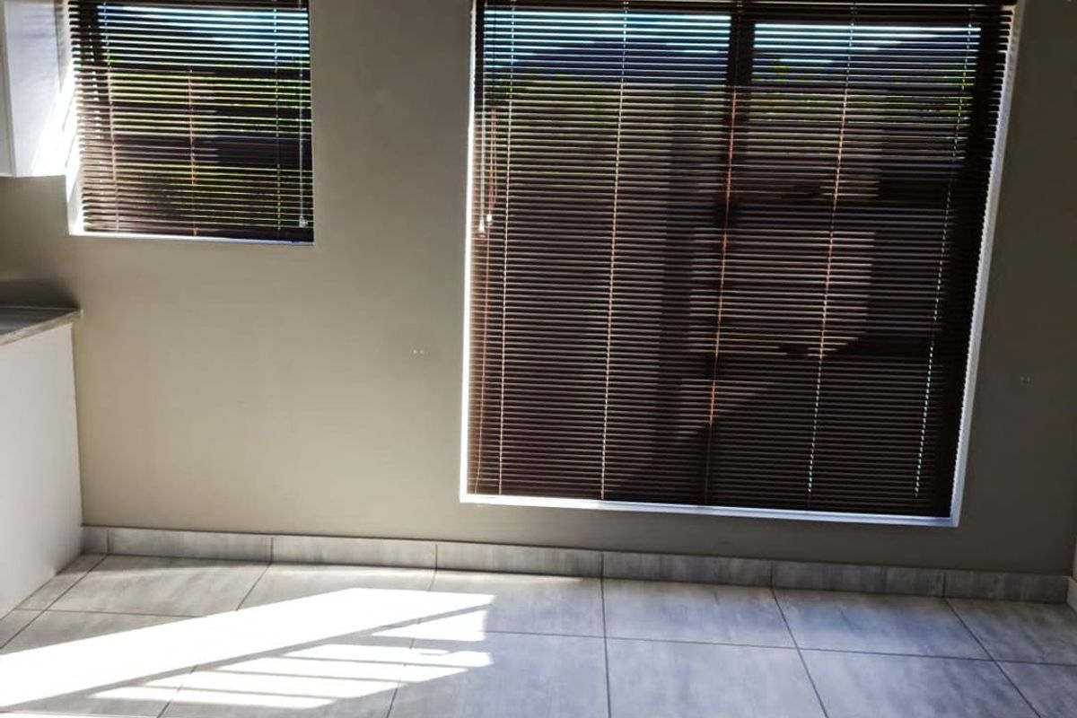 An empty living area featuring neutral wall paint, large windows with fitted venetian blinds, and modern grey tiled flooring.