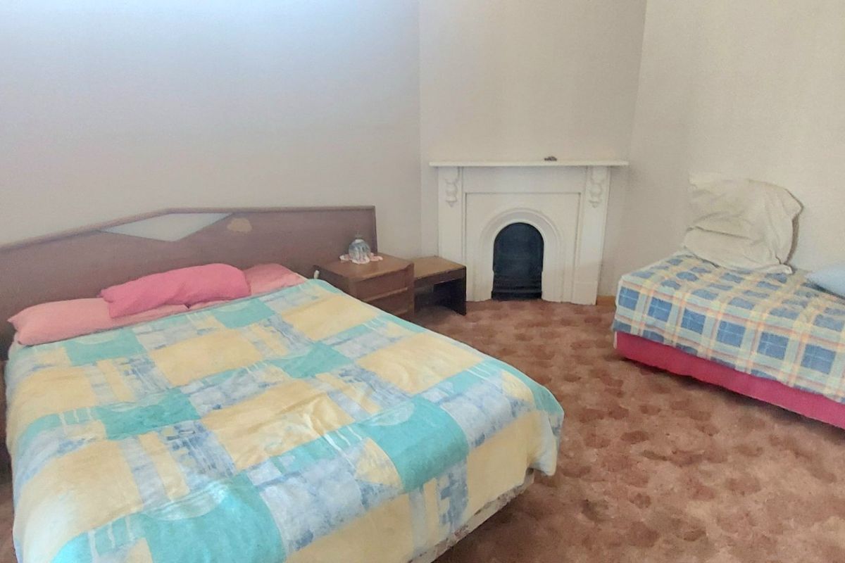 A bedroom featuring a traditional fireplace with a mantelpiece, requiring cosmetic updates to the flooring and finishes to modernize the space.