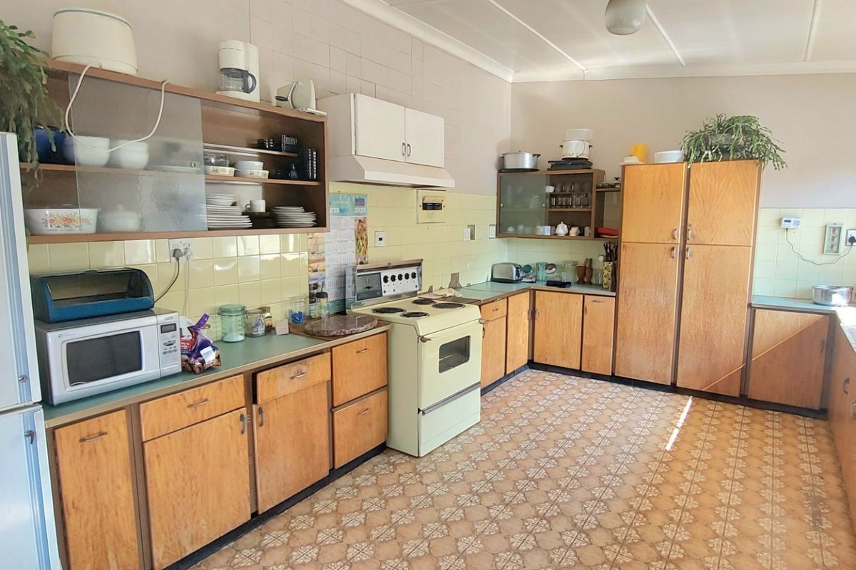 A spacious, dated kitchen featuring original wooden cabinetry, tiled backsplash, and a freestanding stove, offering significant potential for a modern renovation.