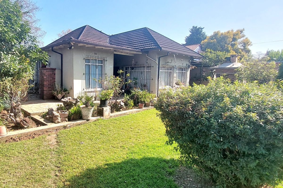 Rear view of the house featuring a tiled roof, security bars on windows, and a paved patio area overlooking the garden.