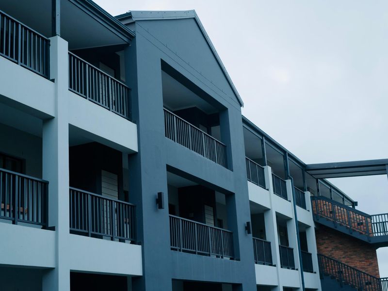A modern apartment building exterior featuring multi-level balconies with metal railings and a combination of painted cladding and brickwork finishes.