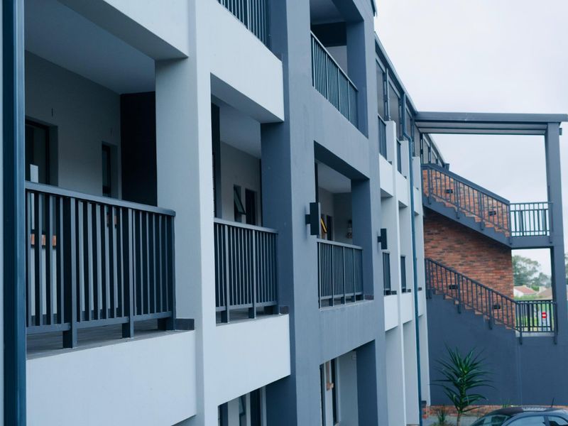 Modern apartment building exterior featuring multi-level balconies with metal railings and an external staircase with brick detailing.