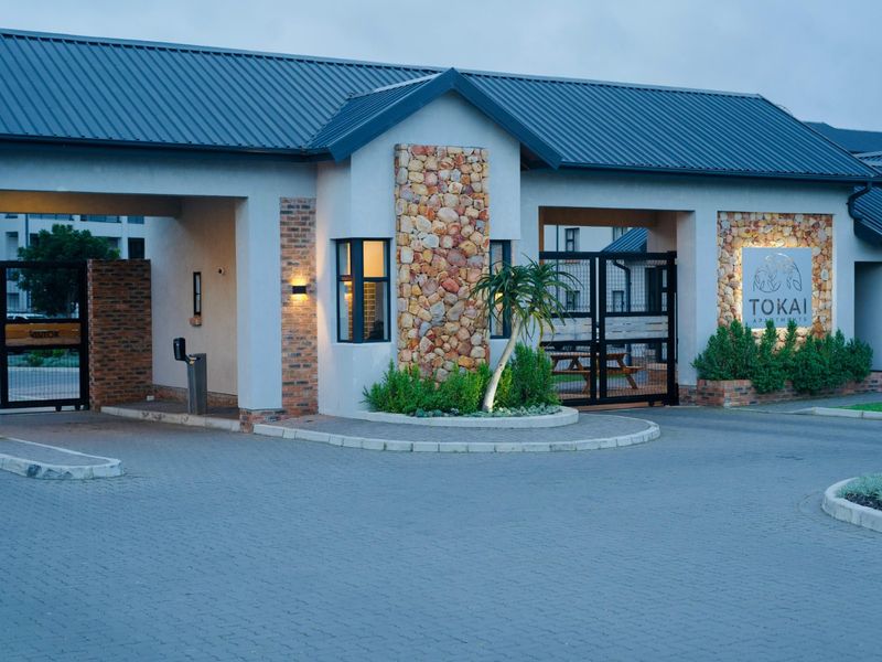 The main entrance and security gatehouse of Tokai Apartments, featuring stone cladding, brick accents, and a paved driveway.