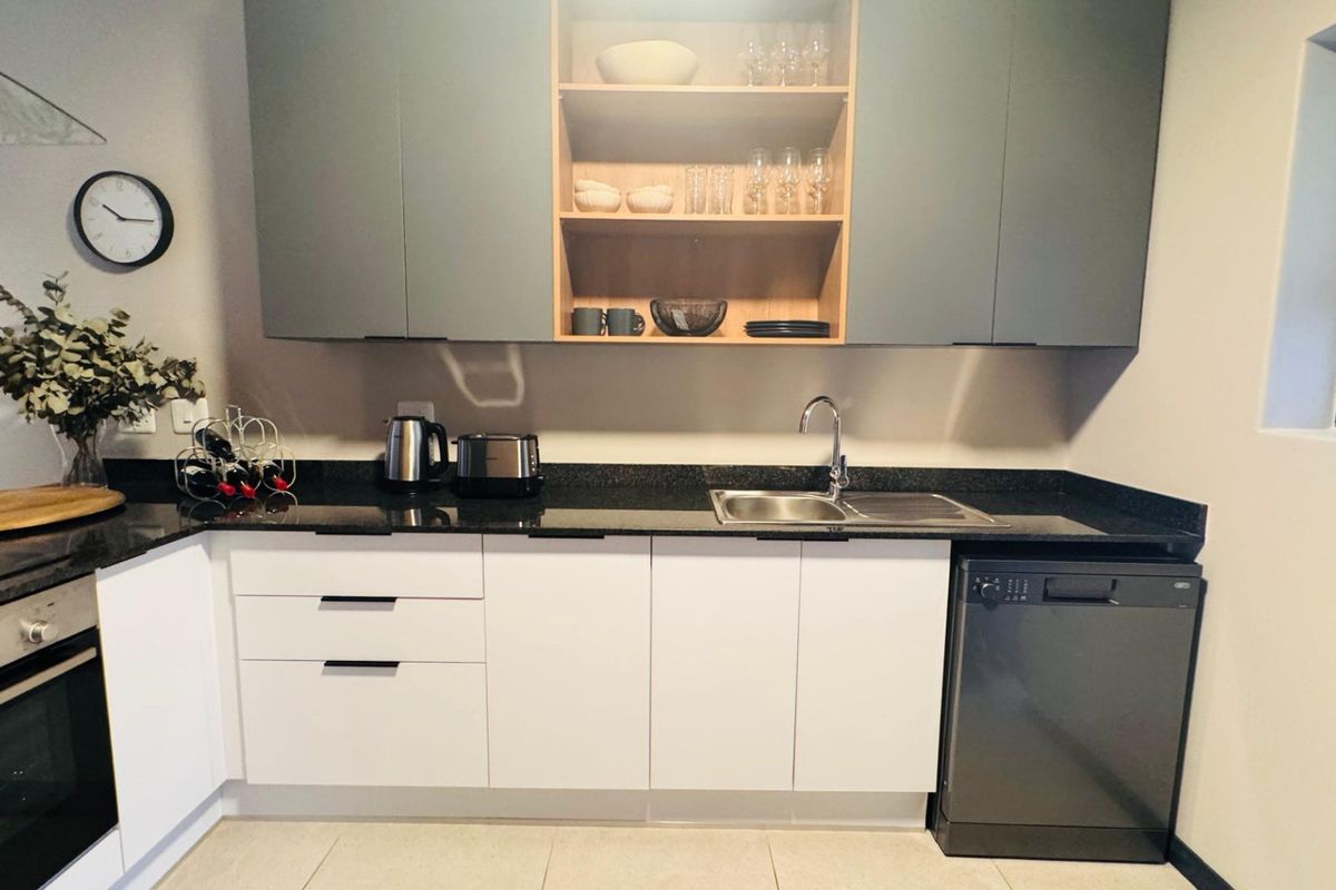 Modern kitchen featuring sleek two-tone cabinetry, granite countertops, built-in oven, and integrated dishwasher, offering a clean and functional workspace.