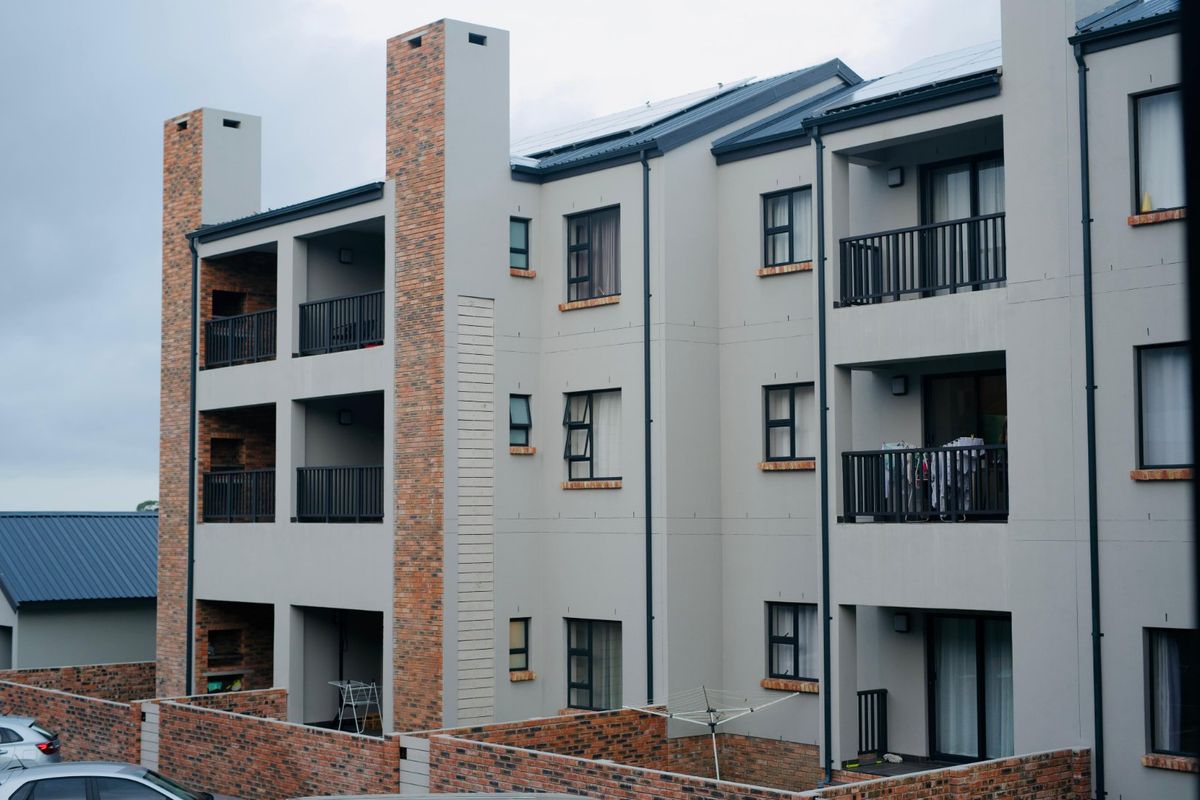 Rear view of a modern multi-story apartment complex featuring brick accents, private balconies with metal railings, and solar panels on the roof.