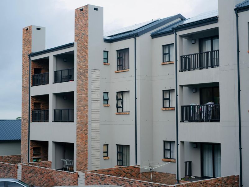 Rear view of a modern multi-story apartment complex featuring brick accents, private balconies with metal railings, and solar panels on the roof.