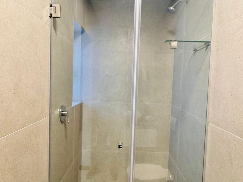 A modern, clean walk-in shower featuring large-format neutral wall tiles, a frameless glass door, and a built-in shower fixture.