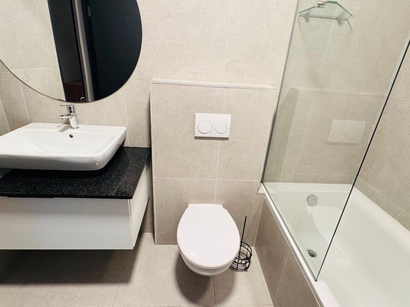 Modern bathroom featuring a wall-mounted vanity with vessel sink, concealed cistern toilet, and a bathtub with a glass shower screen.