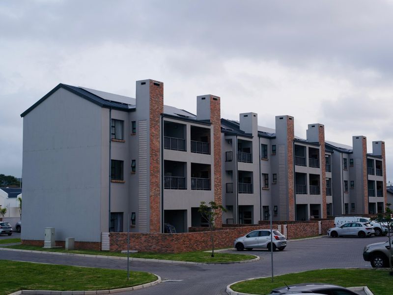 A multi-story apartment complex featuring brick and plaster facade, private balconies with metal railings, and an integrated paved parking area.