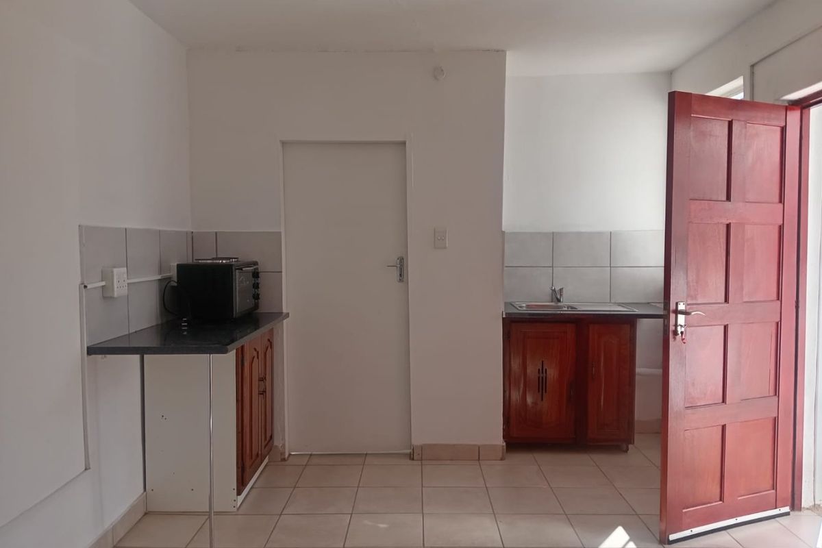 A basic kitchen area featuring tiled flooring, a tiled backsplash, and wooden cabinetry with a sink, offering a functional space for renovation.