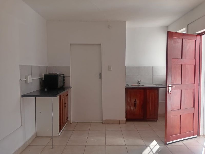 A basic kitchen area featuring tiled flooring, a tiled backsplash, and wooden cabinetry with a sink, offering a functional space for renovation.