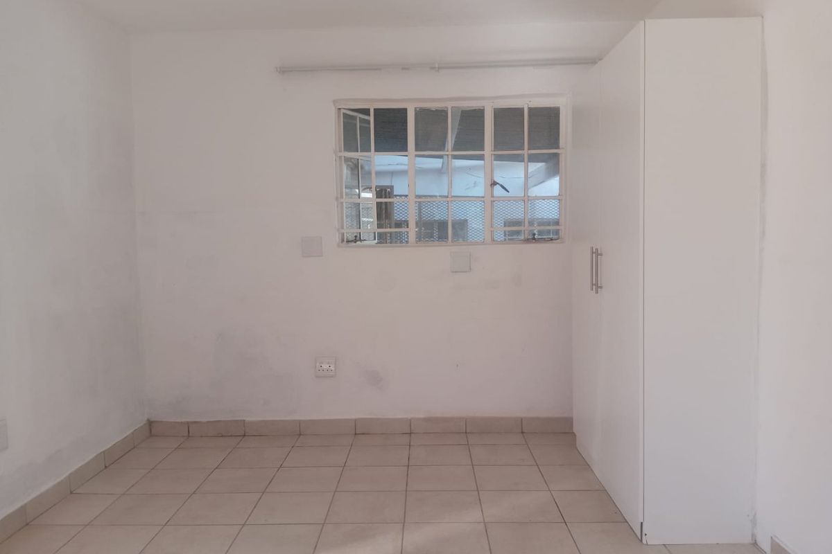 A vacant bedroom featuring tiled flooring, a built-in white wardrobe, and a window fitted with security bars.