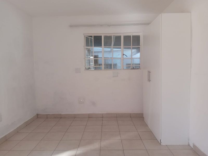 A vacant bedroom featuring tiled flooring, a built-in white wardrobe, and a window fitted with security bars.