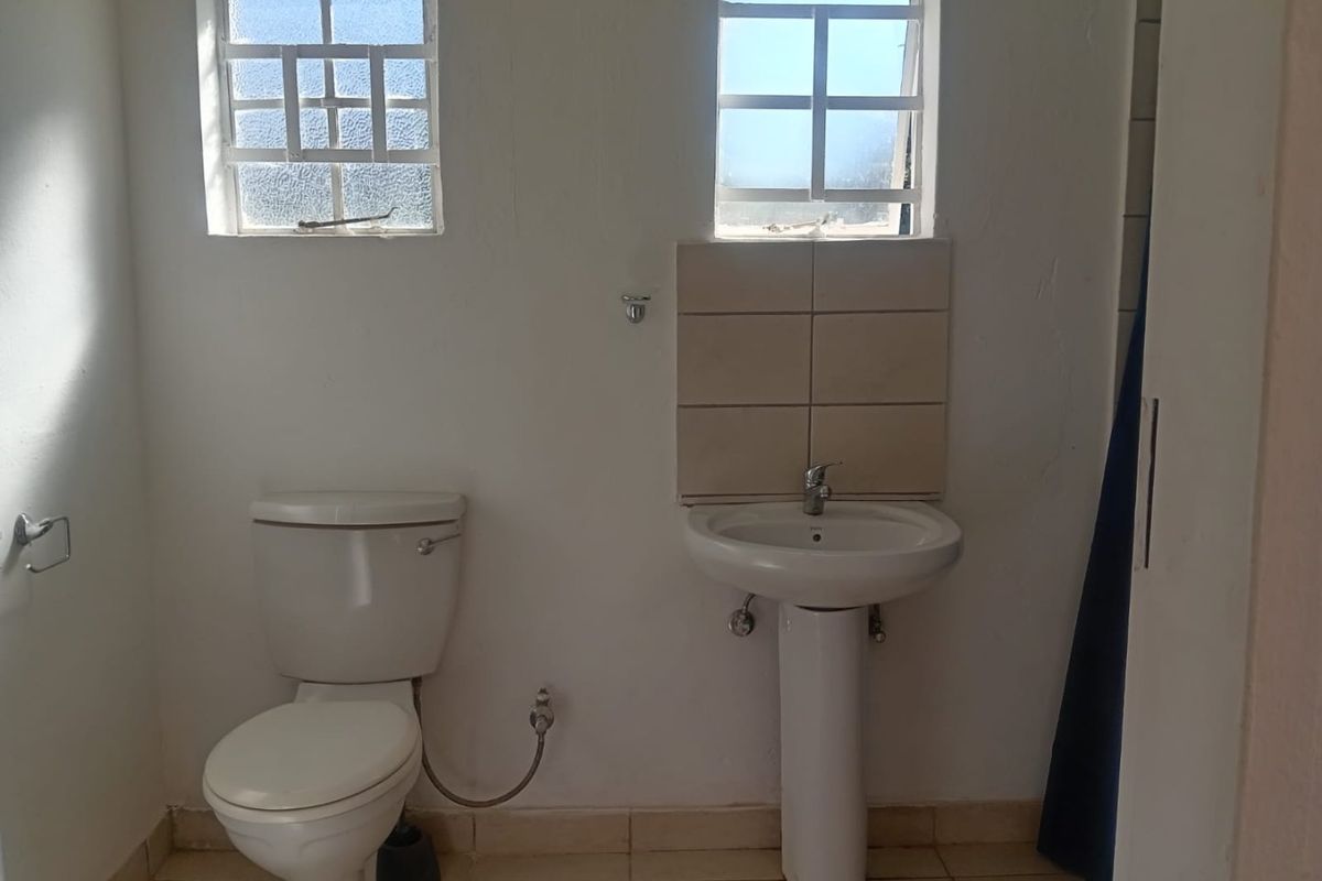 A functional bathroom featuring a pedestal basin, toilet, tiled splashback, and tiled flooring, requiring cosmetic updates to improve its overall condition.