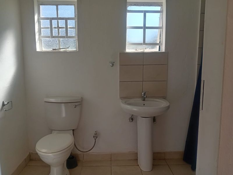 A functional bathroom featuring a pedestal basin, toilet, tiled splashback, and tiled flooring, requiring cosmetic updates to improve its overall condition.