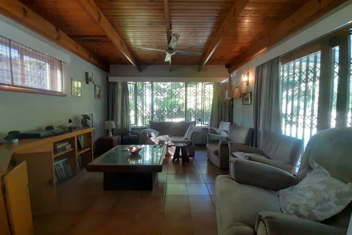 Spacious living room featuring a warm exposed timber beam ceiling, ceramic tiled flooring, and large windows with integrated security gates.
