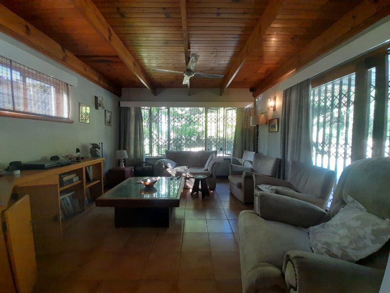 Spacious living room featuring a warm exposed timber beam ceiling, ceramic tiled flooring, and large windows with integrated security gates.
