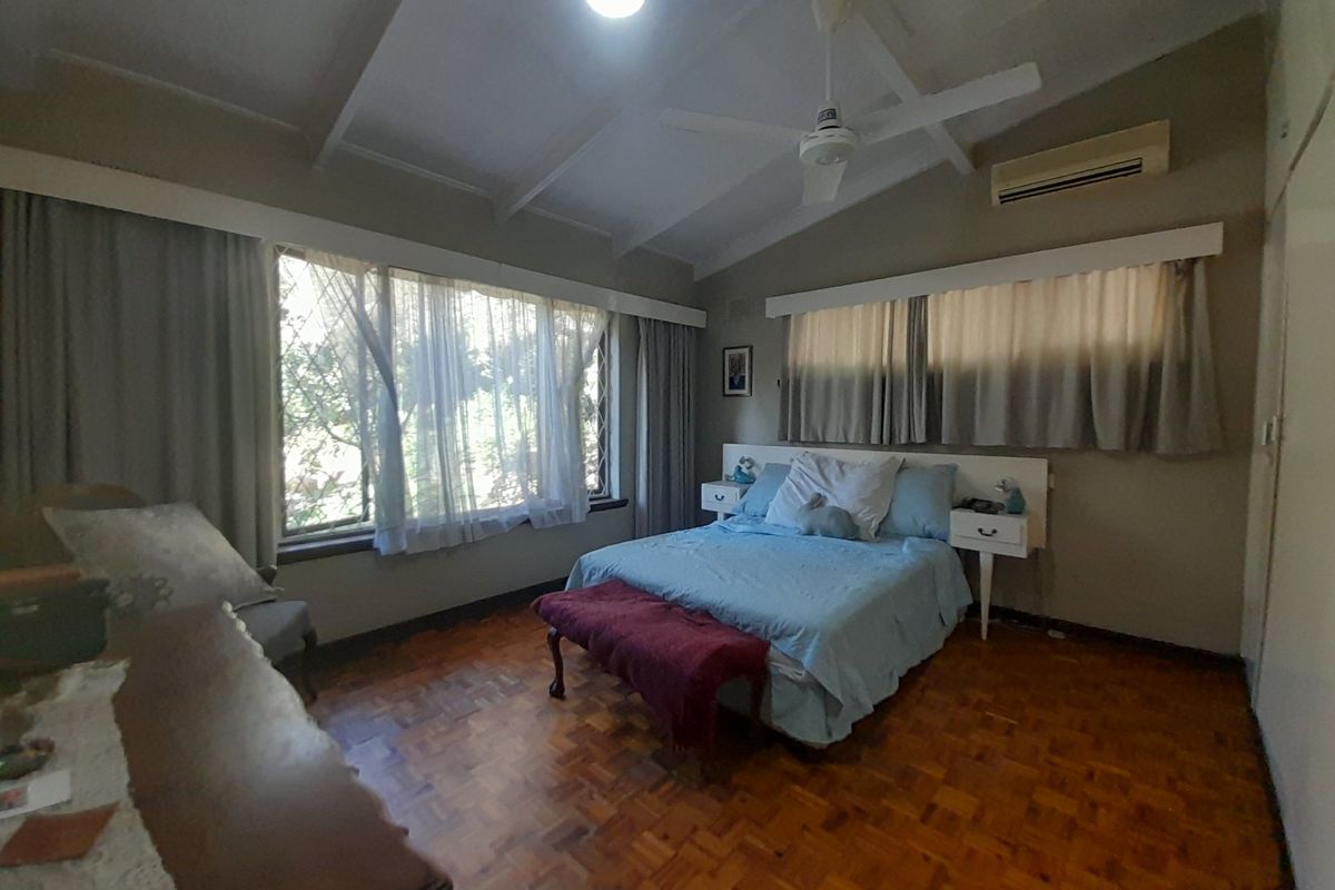 Spacious bedroom featuring warm parquet flooring, a vaulted ceiling with a fan, and a wall-mounted air conditioning unit.