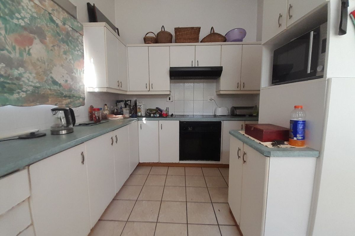A functional kitchen featuring white built-in cabinetry, laminate countertops, tiled flooring, and integrated appliances including an oven and microwave.