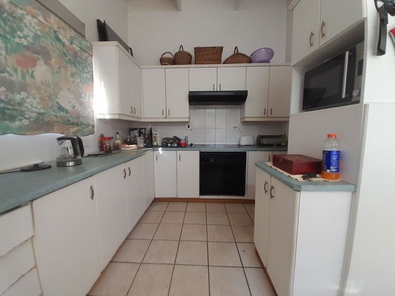 A functional kitchen featuring white built-in cabinetry, laminate countertops, tiled flooring, and integrated appliances including an oven and microwave.