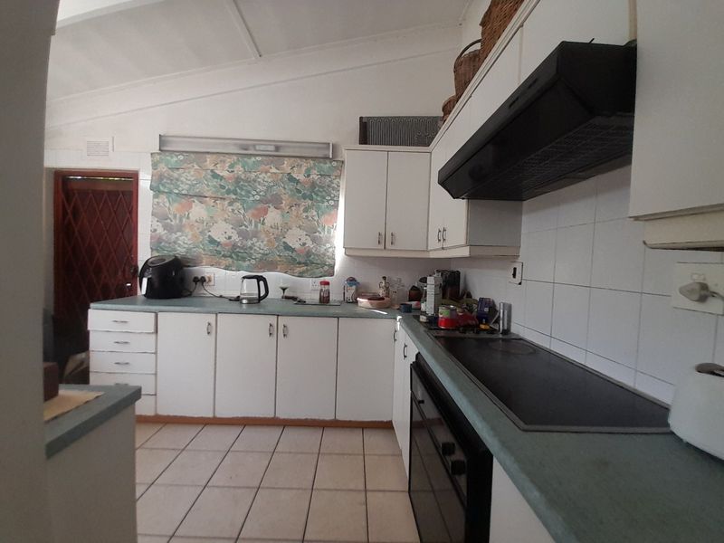 A functional kitchen featuring white cabinetry, laminate countertops, tiled flooring, and built-in appliances including an oven, hob, and extractor fan.