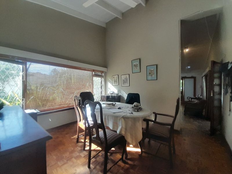 Dining room featuring classic parquet flooring, high ceilings with exposed beams, and a large window providing natural light.