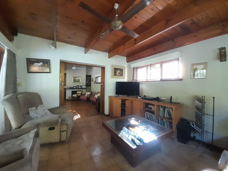Spacious living room featuring a high exposed timber beam ceiling, ceiling fan, tiled flooring, and built-in timber cabinetry.