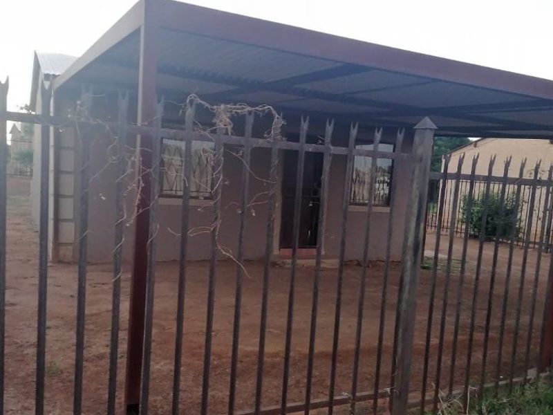 Front view of a residential property featuring a metal carport and perimeter security fencing.