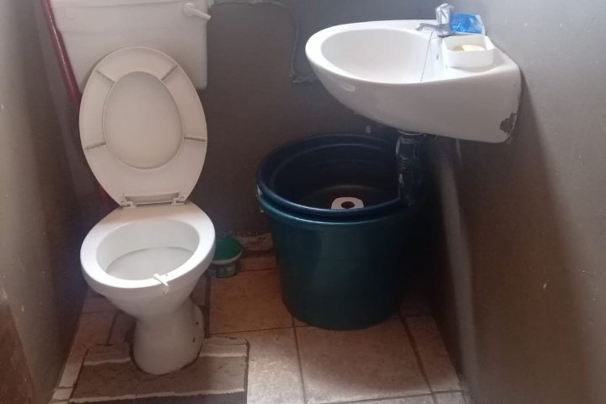 A small bathroom featuring a standard toilet and a wall-mounted basin with tiled flooring, requiring cosmetic updates and maintenance.