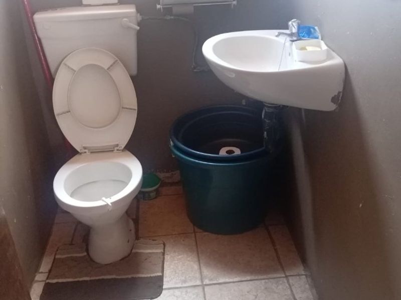 A small bathroom featuring a standard toilet and a wall-mounted basin with tiled flooring, requiring cosmetic updates and maintenance.