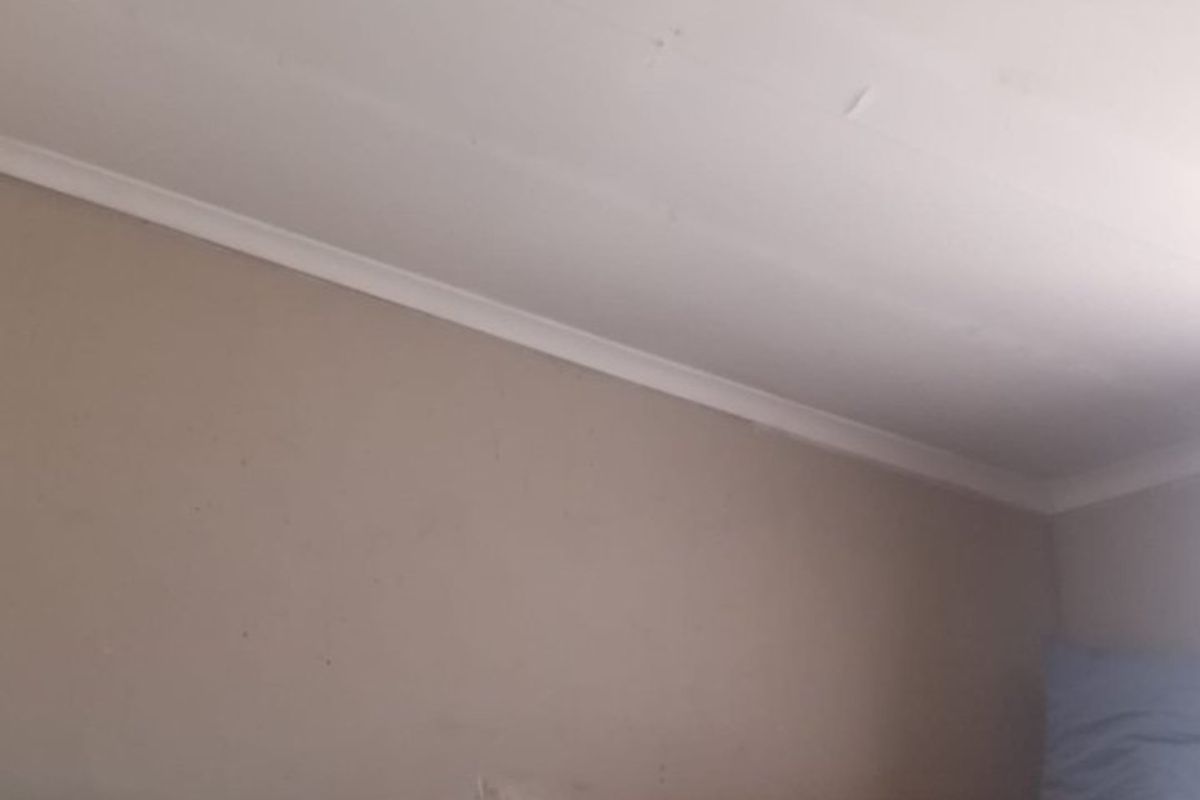 A bedroom interior showing wall and ceiling surfaces with visible signs of wear and cracking in the ceiling joints.