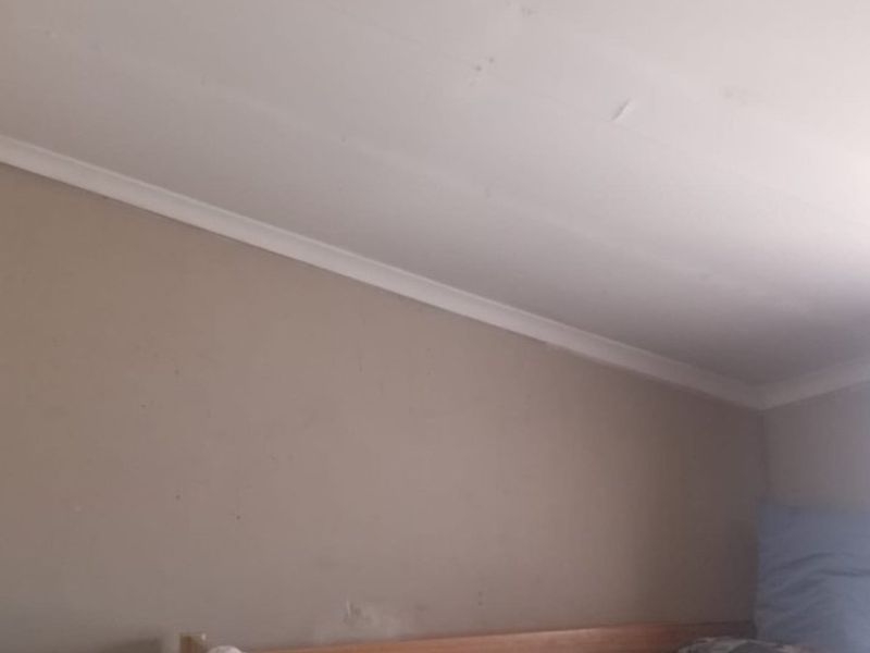 A bedroom interior showing wall and ceiling surfaces with visible signs of wear and cracking in the ceiling joints.