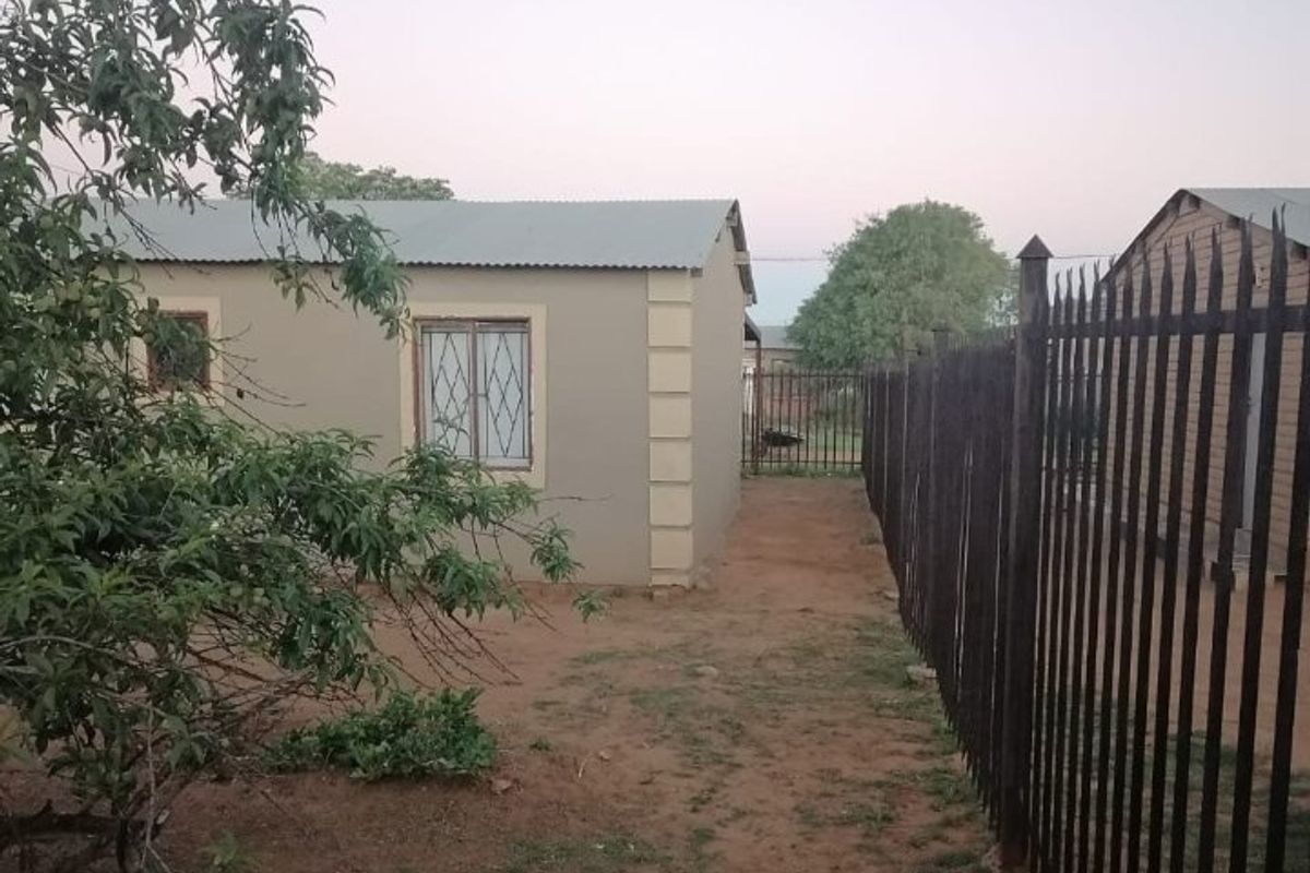 A view of the rear exterior of the property featuring plastered walls, a corrugated metal roof, and metal perimeter fencing.