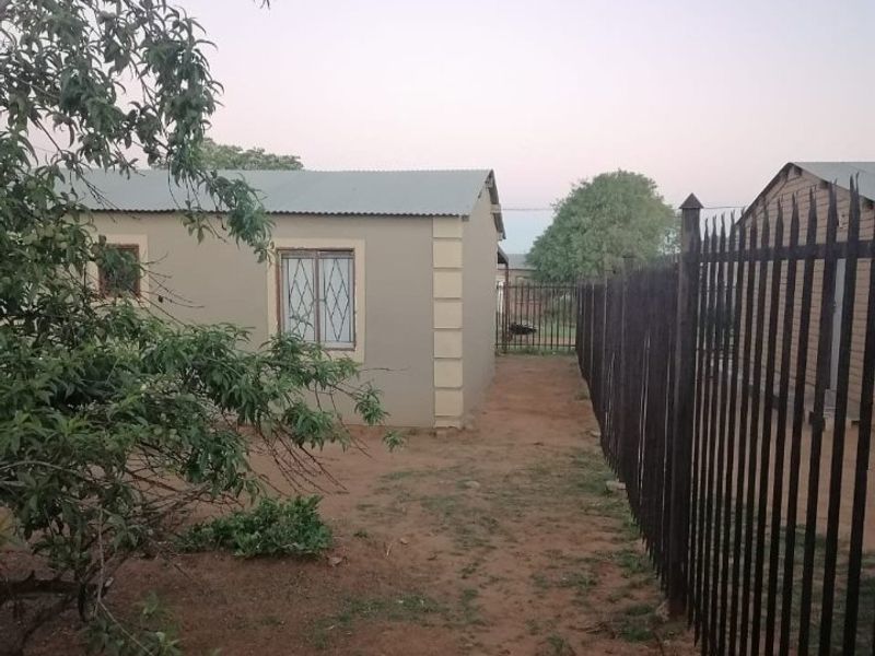 A view of the rear exterior of the property featuring plastered walls, a corrugated metal roof, and metal perimeter fencing.