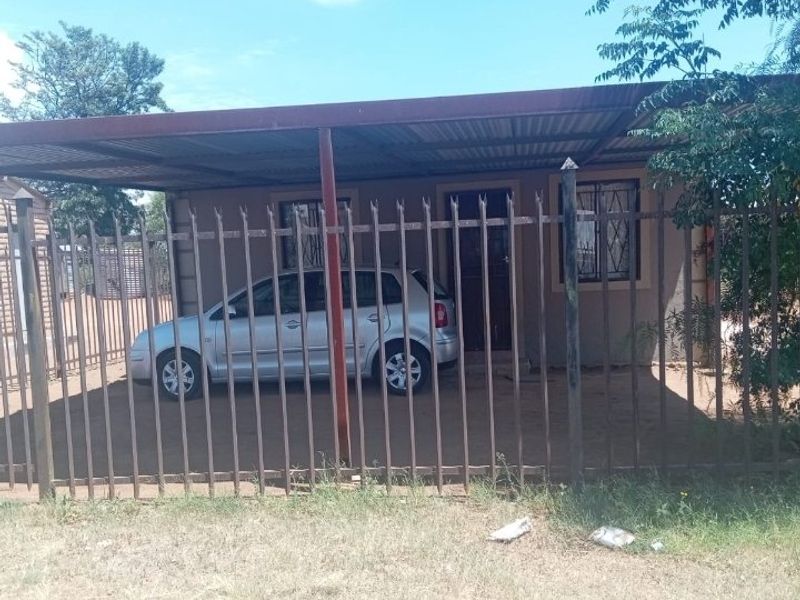 Front exterior view of the property featuring a metal carport, secure steel fencing, and security bars on the windows.