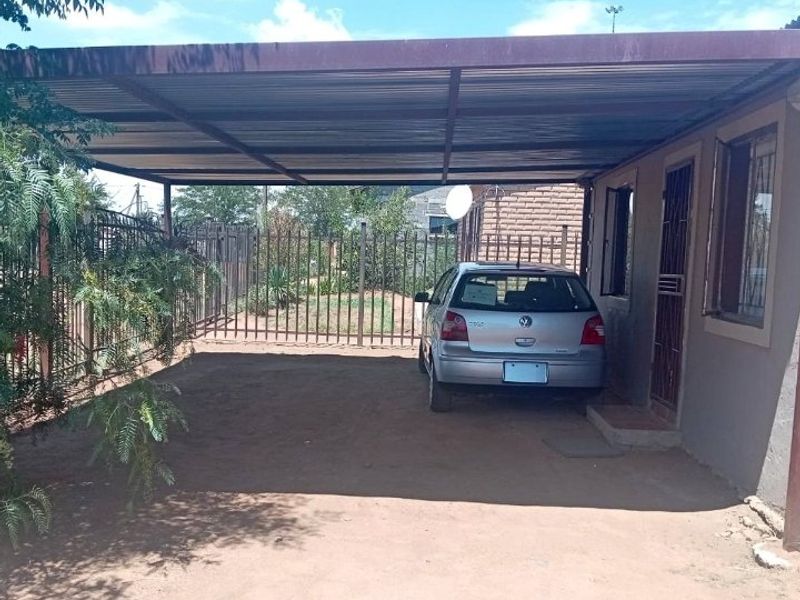 A covered carport area with a metal roof structure and perimeter security fencing.