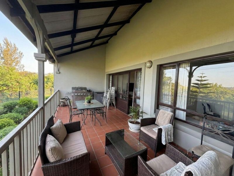 A spacious covered balcony featuring tiled flooring, a protective roof structure, and large sliding glass doors providing access to the interior living area.