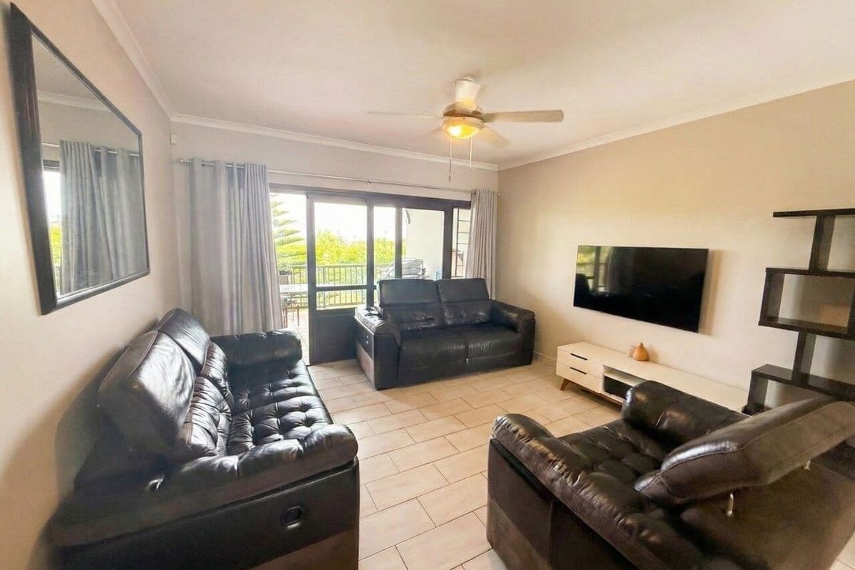A well-maintained living room featuring tiled flooring, a ceiling fan, and large sliding glass doors providing access to an outdoor balcony.