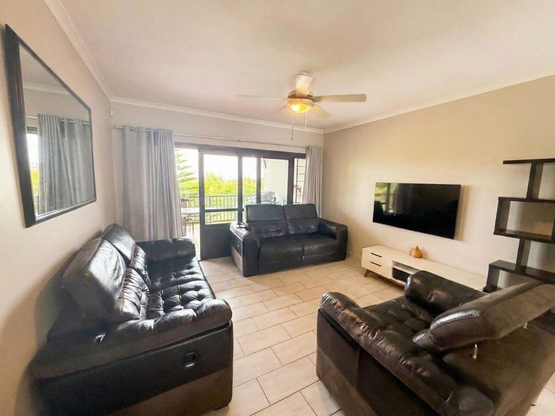 A well-maintained living room featuring tiled flooring, a ceiling fan, and large sliding glass doors providing access to an outdoor balcony.