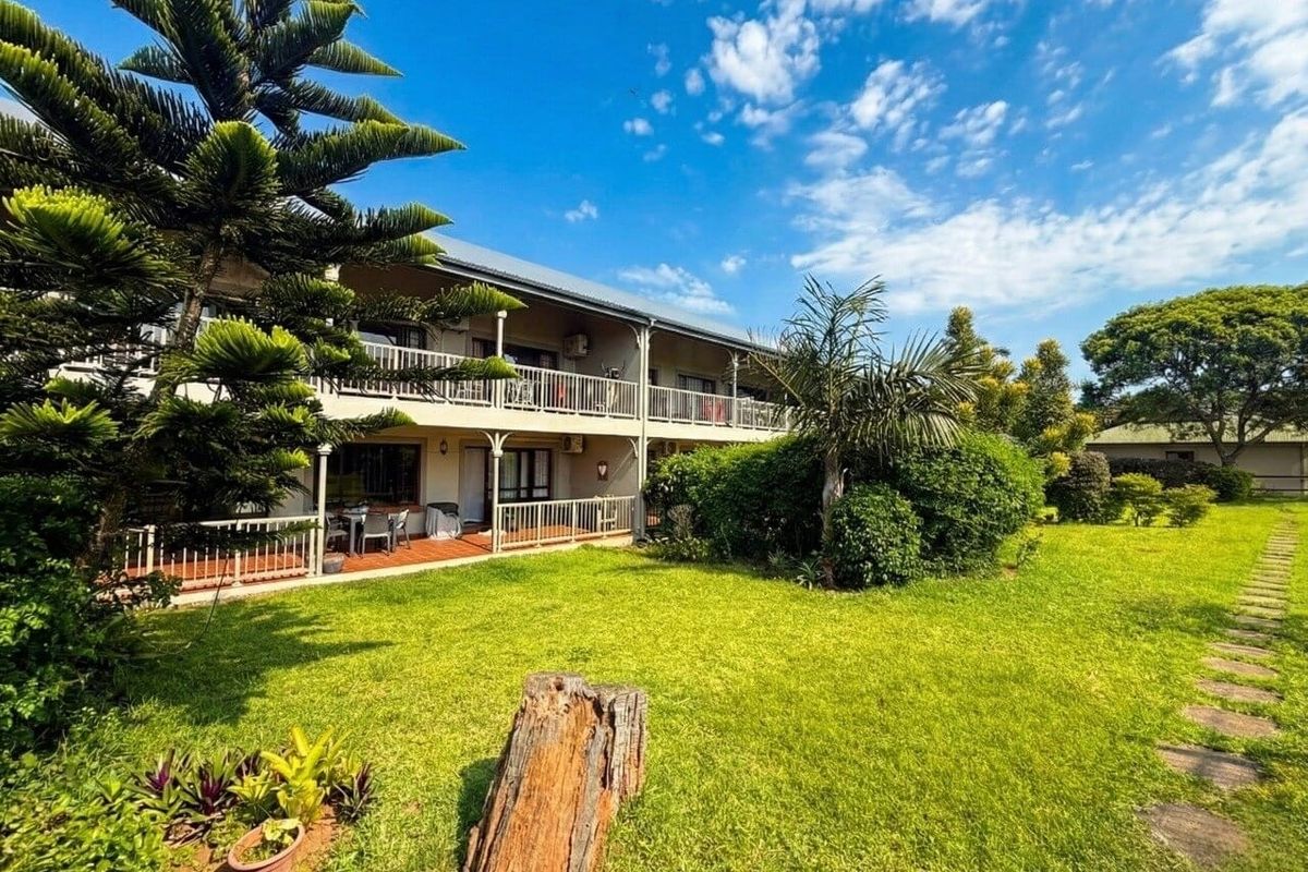 Rear view of the apartment building featuring a landscaped garden, paved walkway, and covered balconies with railings.