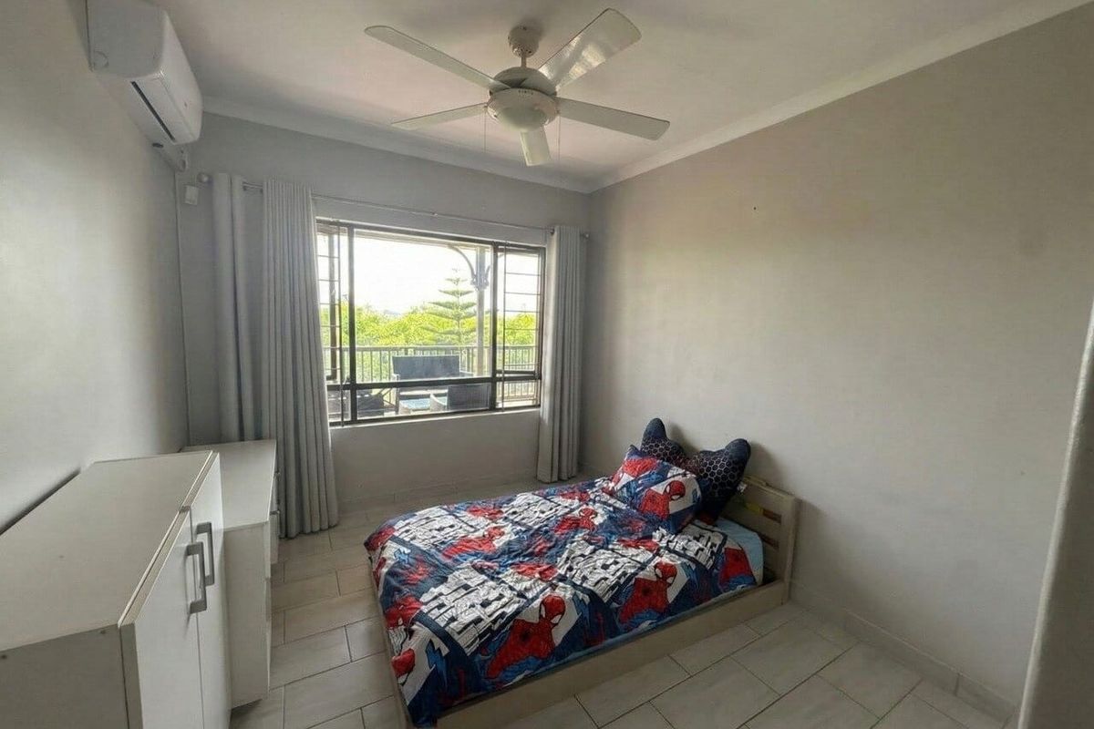 A bedroom featuring tiled flooring, a ceiling fan, and a wall-mounted split-system air conditioner, with natural light provided by a large window.