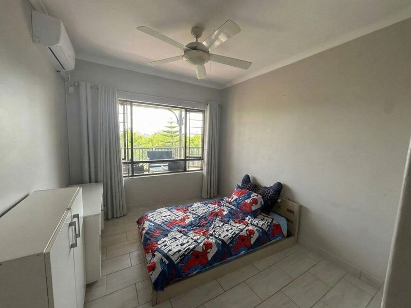 A bedroom featuring tiled flooring, a ceiling fan, and a wall-mounted split-system air conditioner, with natural light provided by a large window.