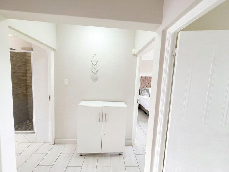 A bright, neutral-toned hallway featuring clean tiled flooring and built-in storage cabinetry, providing access to adjacent rooms.