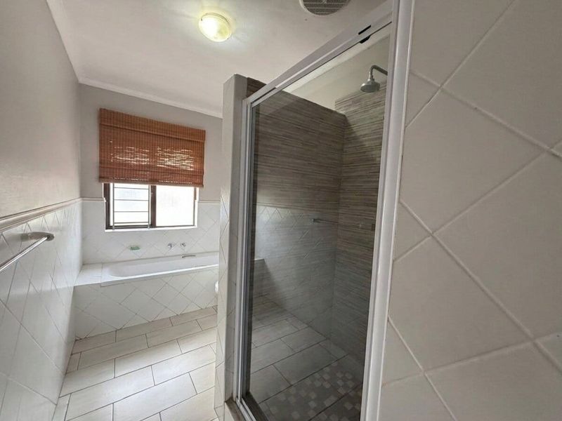 A functional bathroom featuring a built-in bathtub, a separate glass-enclosed shower, and neutral tiled finishes throughout.