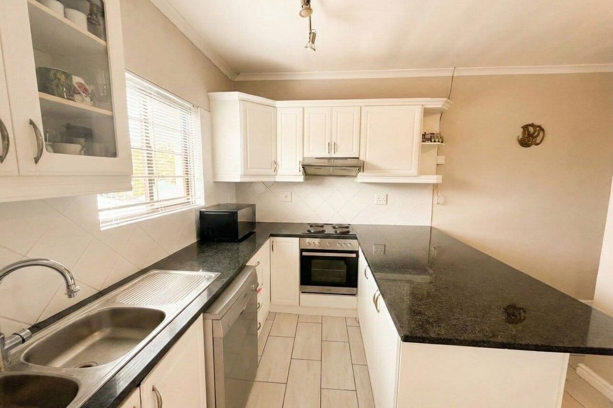 A functional kitchen featuring white cabinetry, dark granite countertops, a built-in oven with hob, and a stainless steel sink.