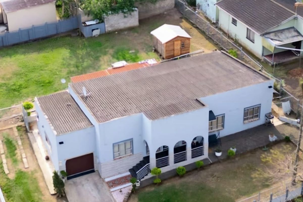 Aerial view of a single-story residential property featuring a corrugated metal roof, arched veranda, and a detached garden shed on a fenced plot.